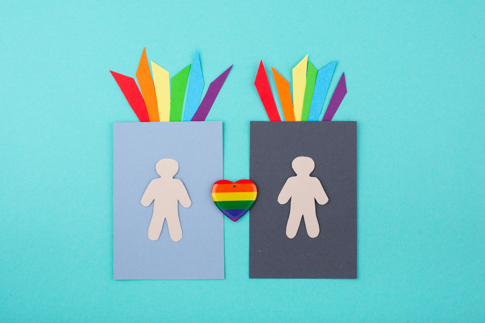 Two paper cutout figures with rainbow colored paper and a rainbow heart between them